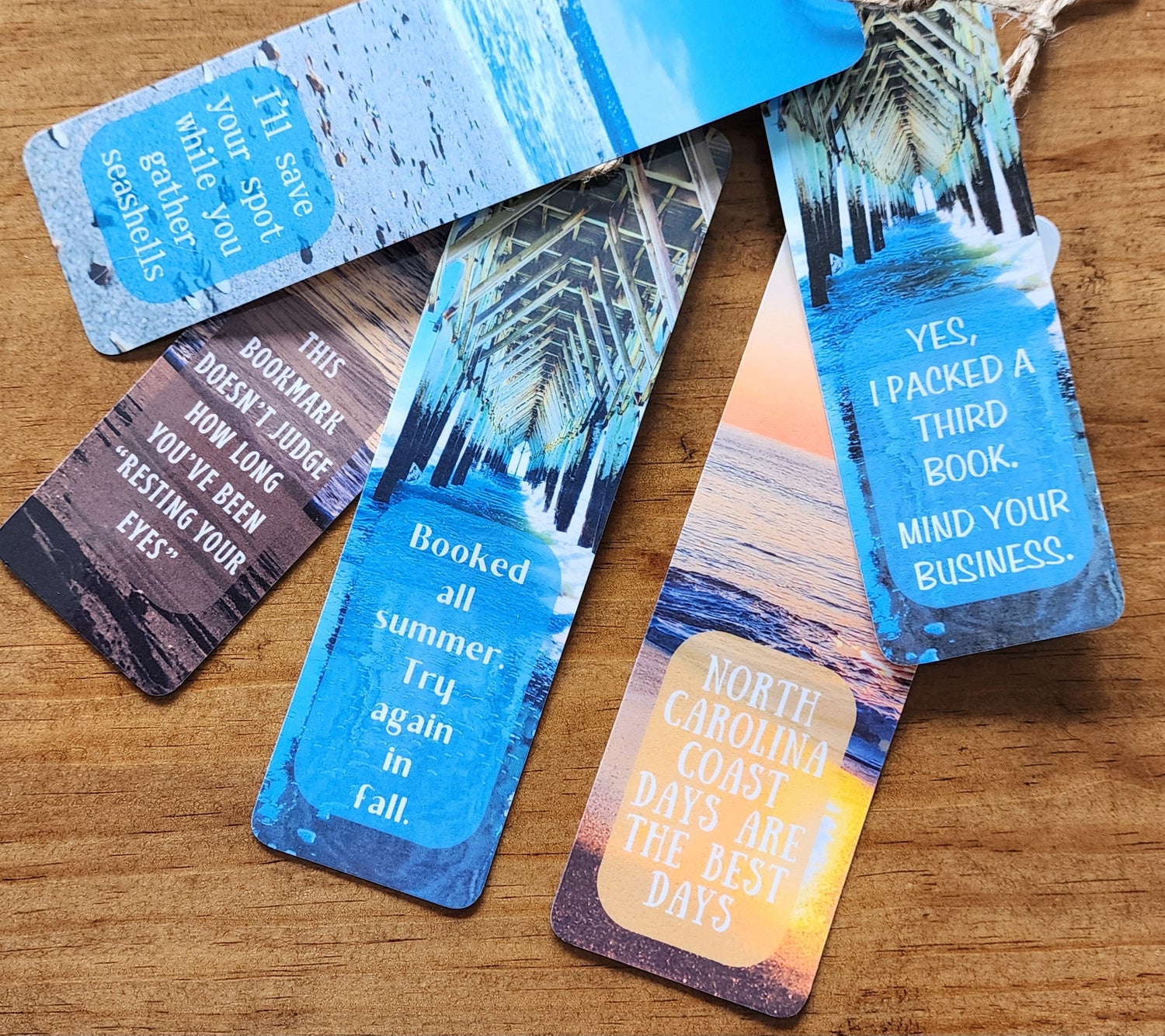 Beachy bookmarks with blue ocean, sunrise and sunset illustrations, featuring humorous quotes like 'This bookmark doesn't judge how long you've been resting your eyes', 'Yes, I packed a 3rd book, mind your business' and 'Booked all summer try again in fall.