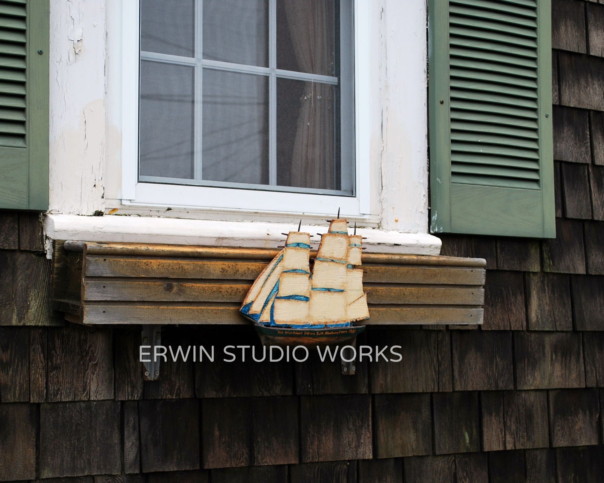 Wooden ship model on a window sill with green shutters and wooden wall.